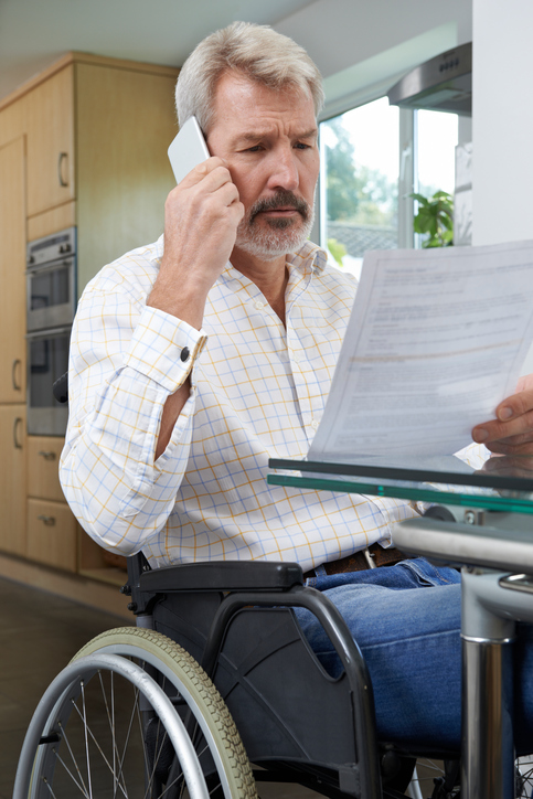 Frustrated Man In Wheelchair Making Phone Call Whilst Reading Le