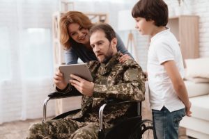 The veteran in a wheelchair came back from the army. A man in uniform in a wheelchair with his family.