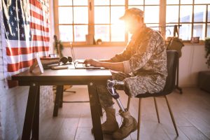 oung Soldier in uniform with amputee leg sitting on desk in office, using lap top